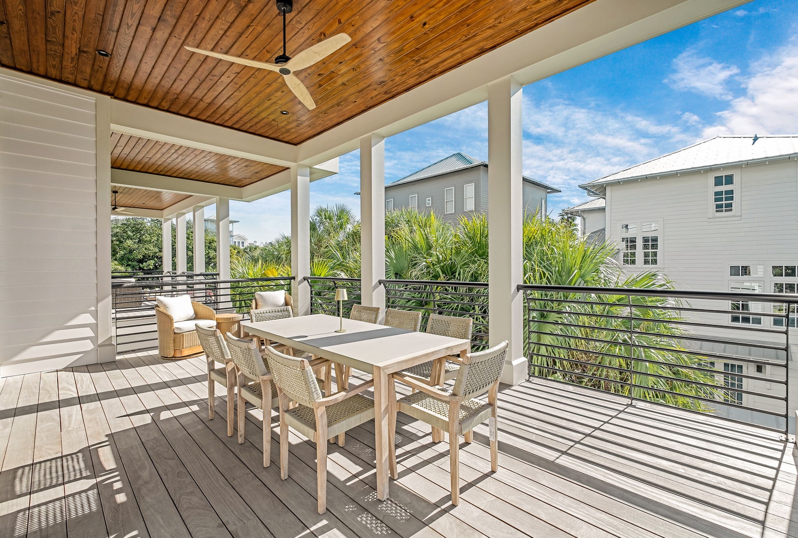 Your private covered deck awaits with dining for six, modern railings, and peaceful neighborhood views beyond tropical palms.