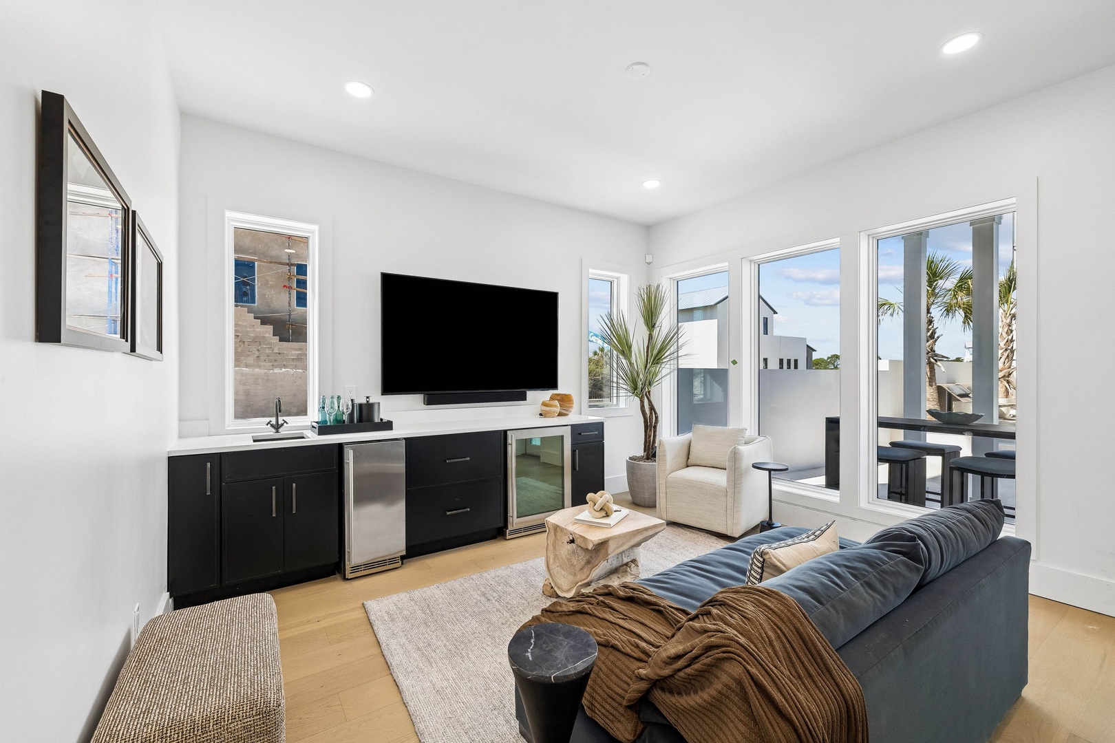 Your bright, modern retreat opens to a private terrace with swaying palms, where sunlight pours through floor-to-ceiling windows and sleek black cabinetry holds a wine fridge ready for evening toasts.