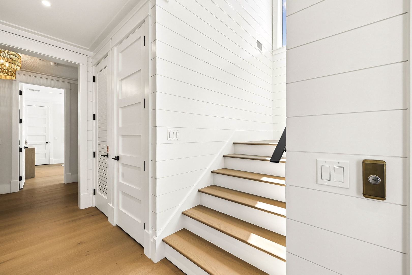 Bright open hallway with coastal-inspired white shiplap walls and gleaming wood floors that guide you upstairs, creating a crisp, airy flow throughout your home.