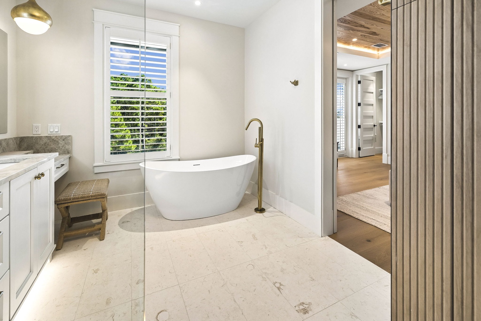 Soak in your elegant freestanding tub with natural light streaming through plantation shutters, then step into the open glass shower. Warm wood accents and marble floors create a spa-like sanctuary you'll love returning to.