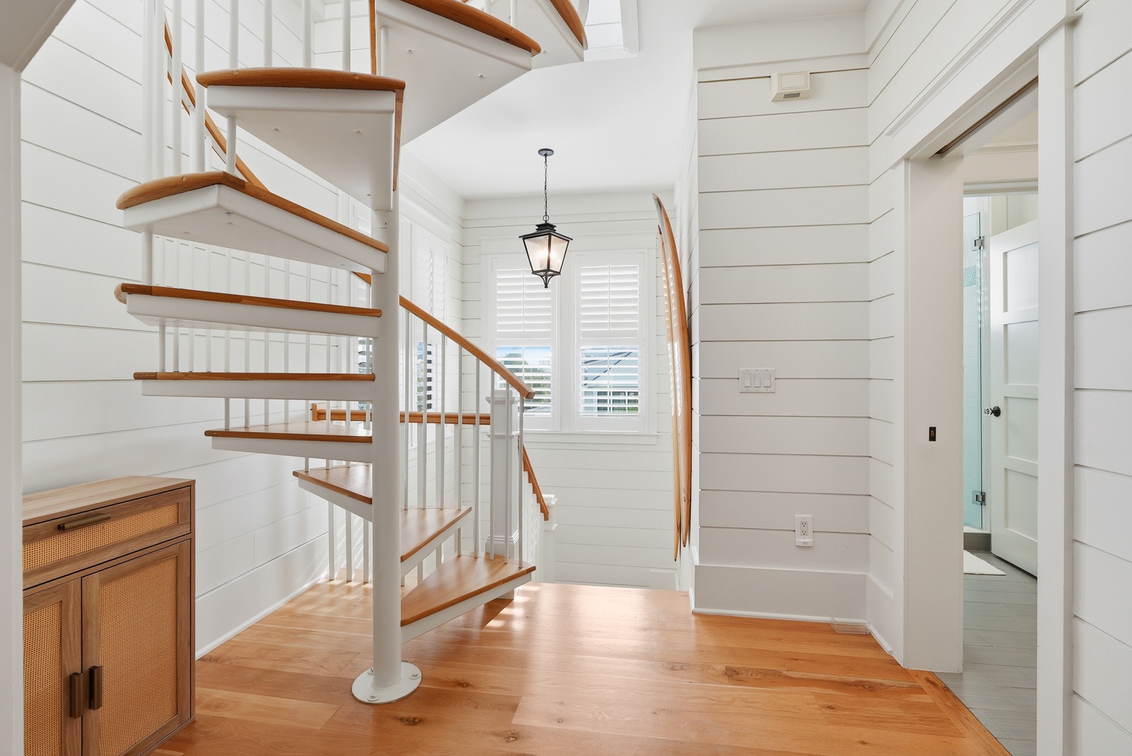 Bright shiplap walls surround a spiral staircase with warm wood tones, offering charm and flow throughout your coastal retreat.