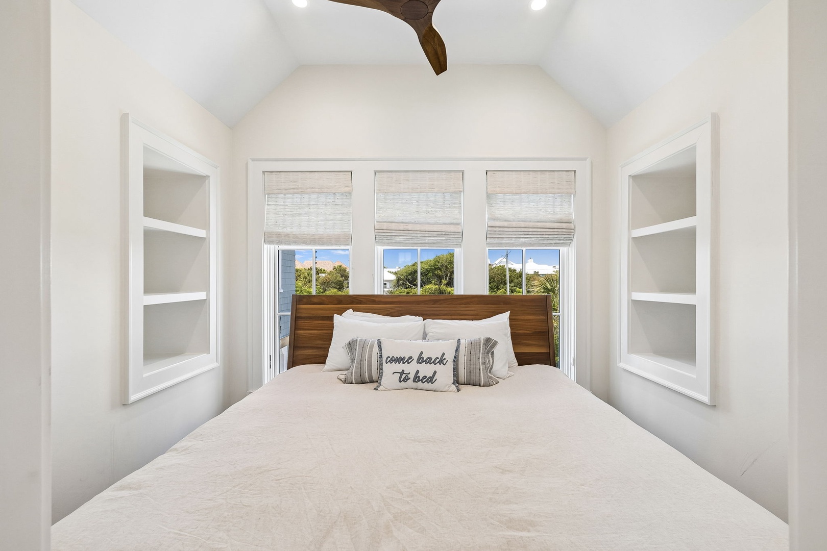 Drift off in this peaceful bedroom, where vaulted ceilings and charming built-in shelves create a cozy sanctuary. Your private retreat awaits with natural light and lush outdoor views.