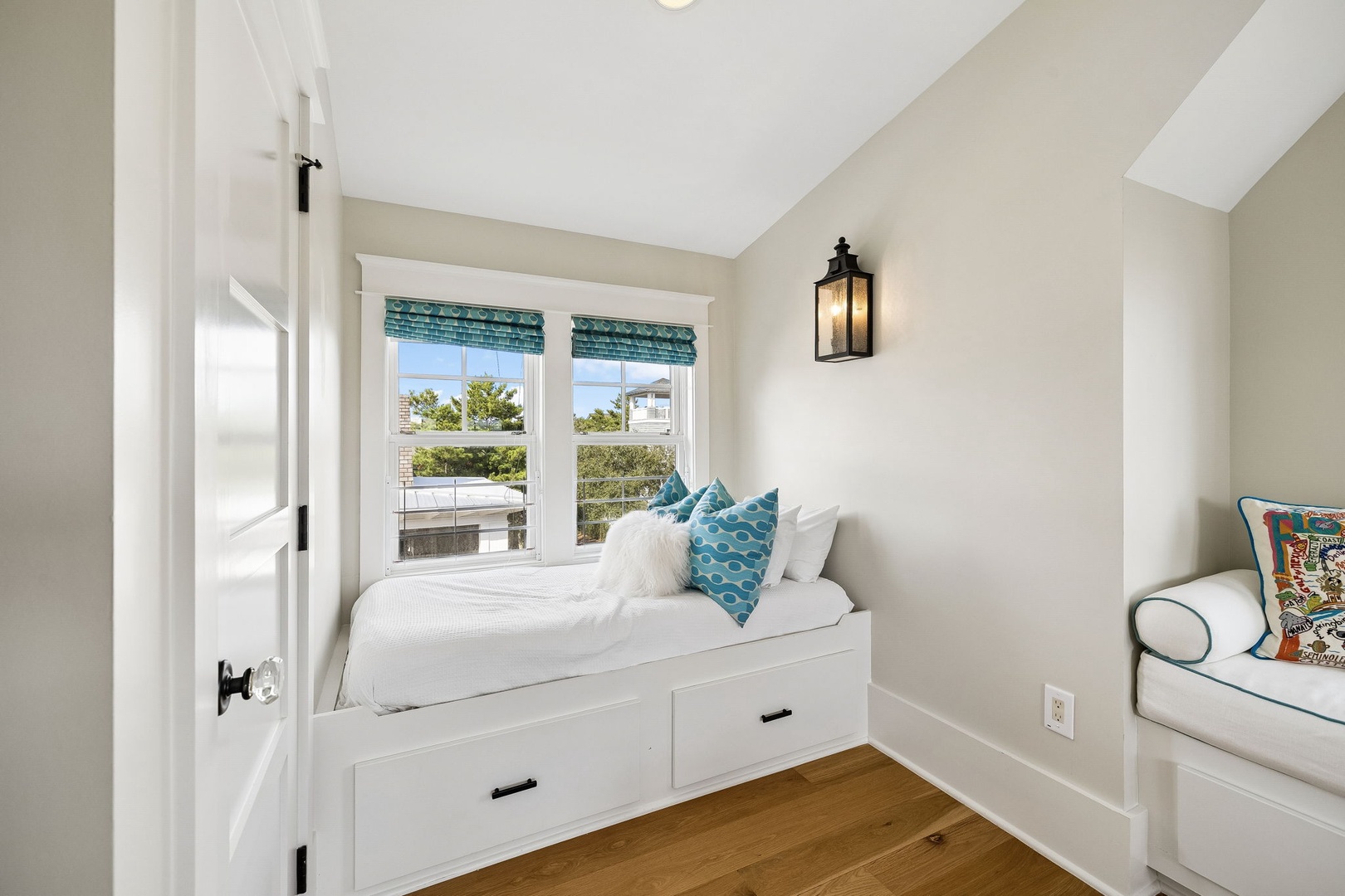 Cozy built-in bed with storage drawers welcomes you to unwind, while bright windows frame leafy neighborhood views and a charming wall sconce adds a warm glow.