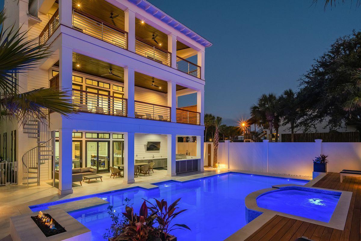 Modern luxury property featuring illuminated pool area and hot tub during evening hours, surrounded by tropical landscaping.