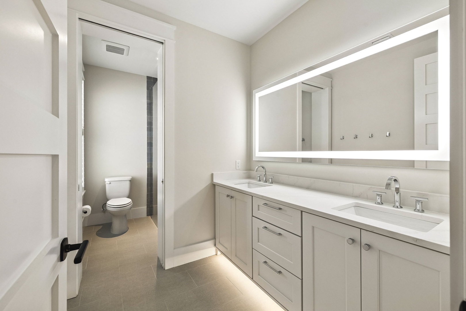 Step into your sleek, modern bathroom featuring dual sinks with elegant fixtures and a backlit mirror that adds a soft, welcoming glow to your morning and evening routines.