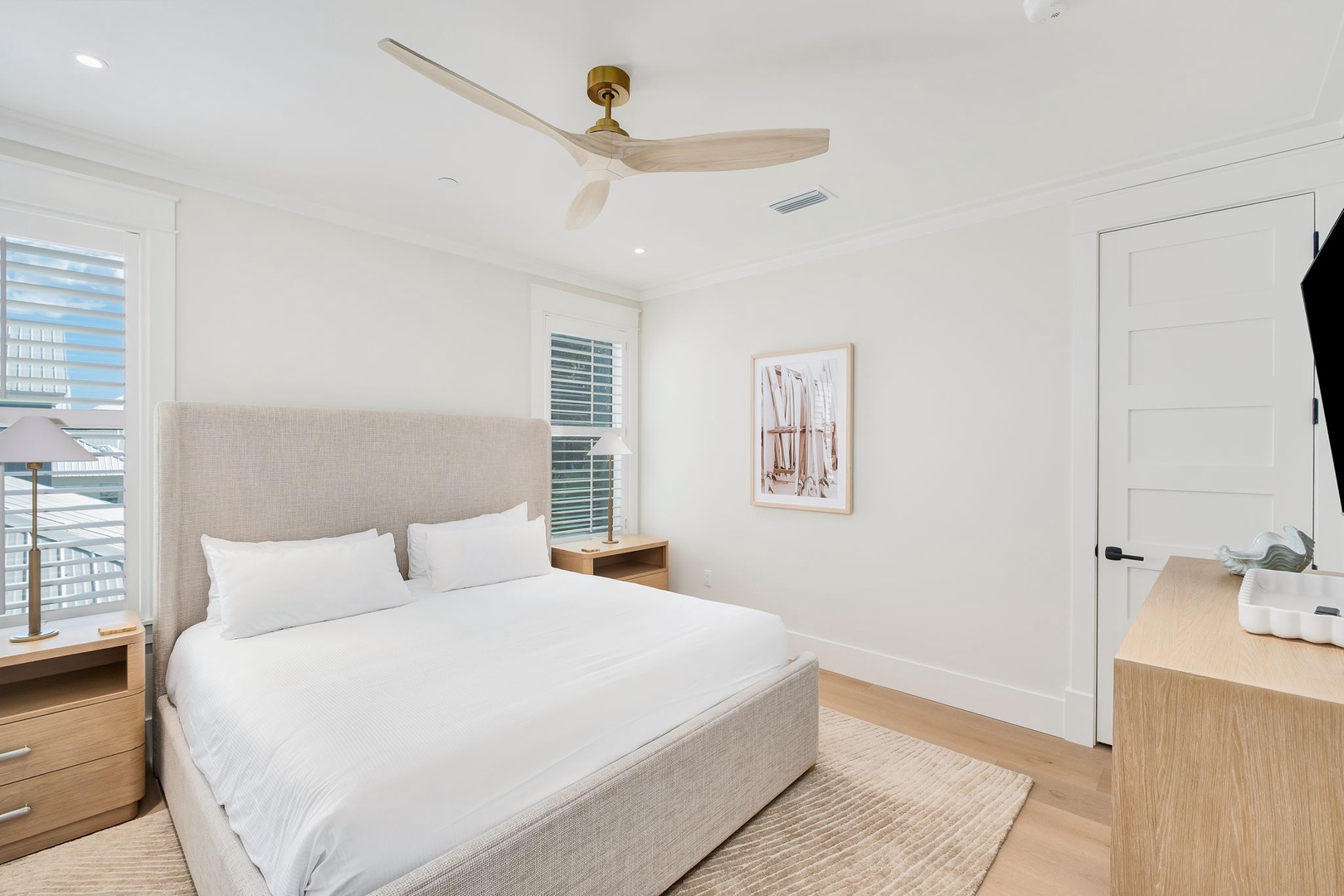 Sink into crisp white linens and enjoy the gentle breeze from the ceiling fan above. This bright, peaceful bedroom is your private retreat, where natural light and coastal calm invite you to unwind.