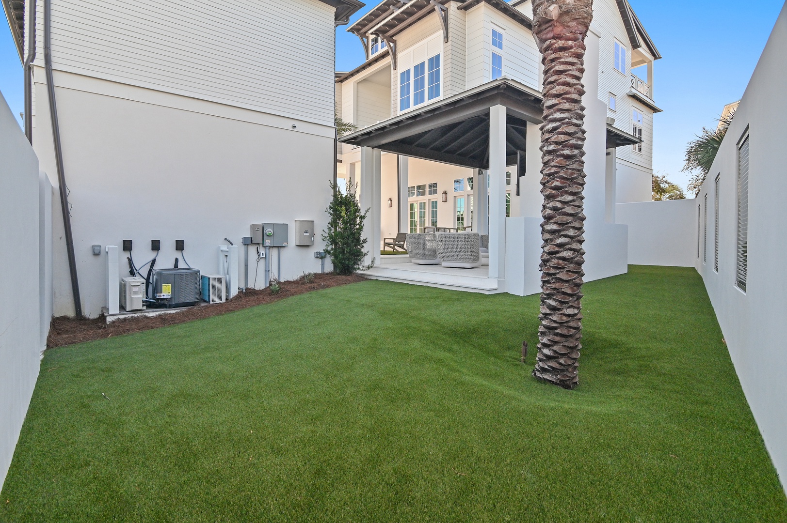 Coastal retreat featuring lush lawn, palm tree, and covered outdoor seating area in a private courtyard setting surrounded by modern architecture.