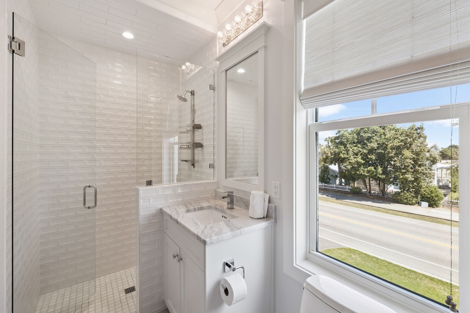 Refresh in your sleek bathroom featuring a spacious glass shower, marble vanity, and beautiful natural light from the large window.