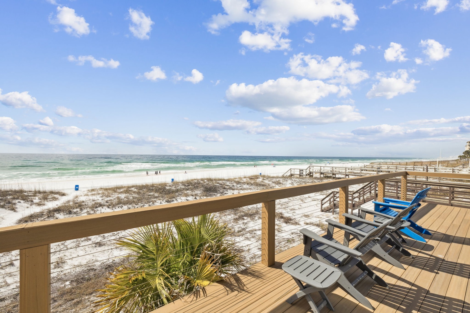 Spacious deck overlooking pristine white sand beach with comfortable seating for relaxing as ocean waves roll in under endless blue skies.