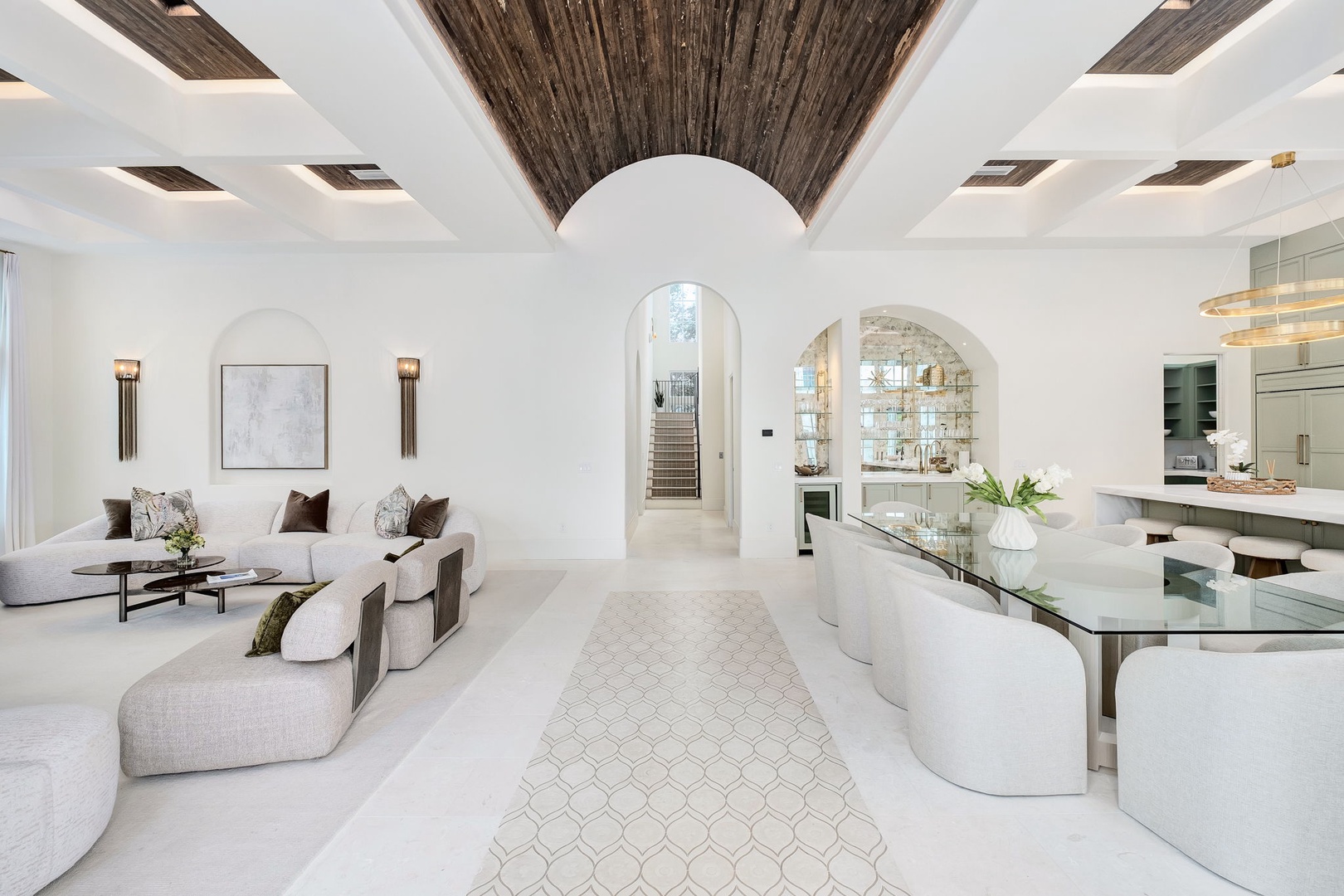 Sink into plush white seating beneath dramatic wooden beams in this light-filled living space. Elegant arched doorways and thoughtful lighting create a sanctuary where modern luxury meets timeless design.