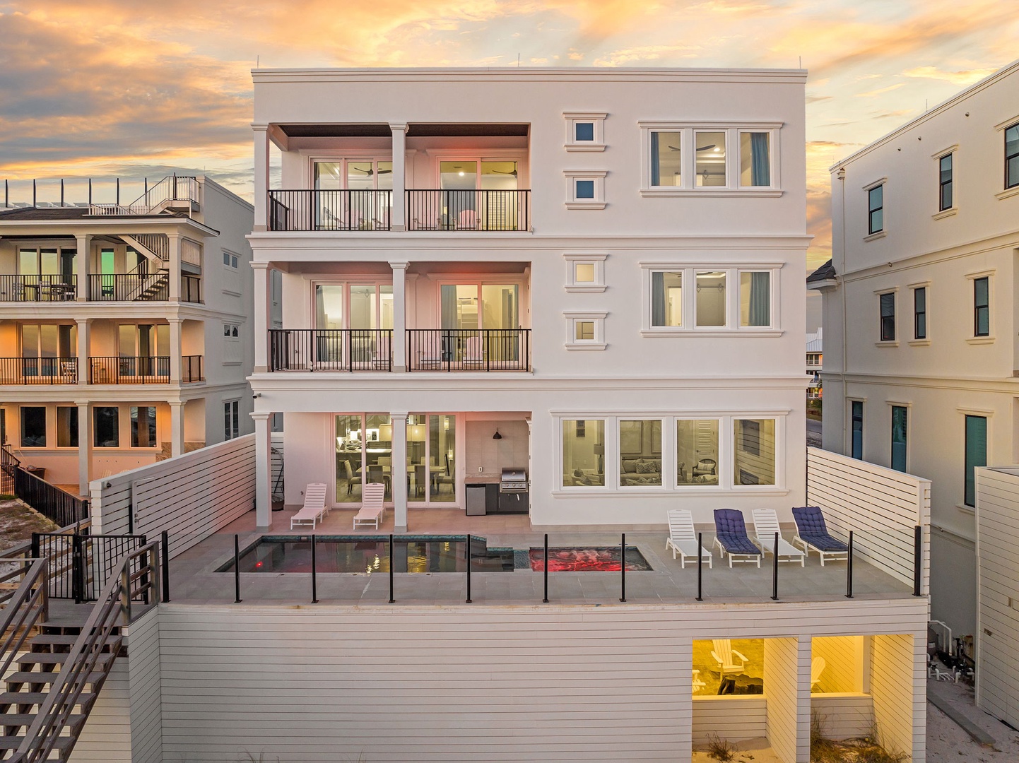 Modern coastal home featuring three levels, private pool deck, and multiple balconies set among neighboring beach houses at sunset.