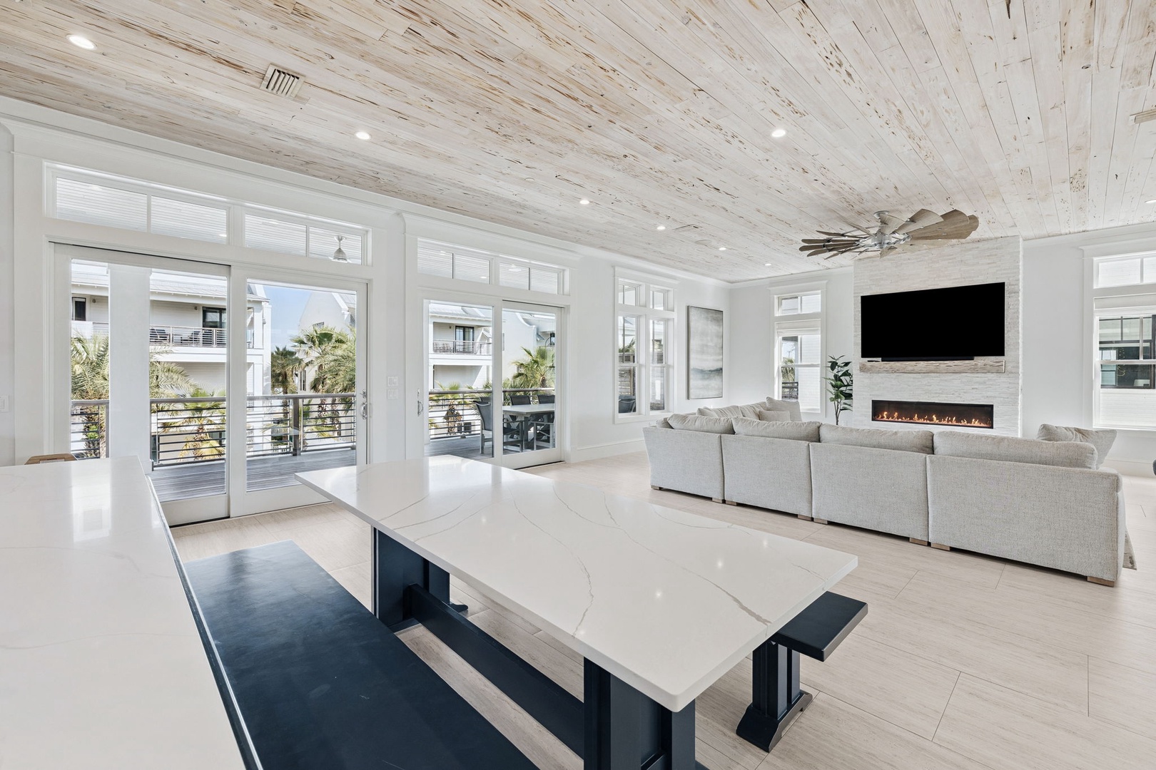 Relax in your stunning open-plan living space featuring soaring whitewashed ceilings, a sleek fireplace, and seamless outdoor patio access.