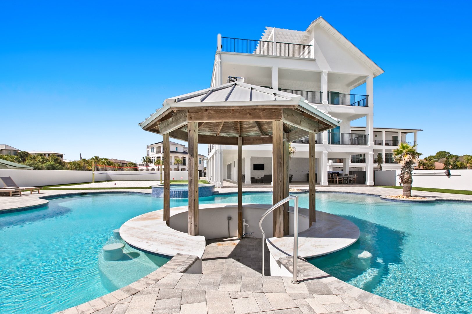 A stunning coastal retreat featuring a multi-level beachfront home with expansive balconies overlooking a resort-style pool with unique swim-up gazebo and bar area.