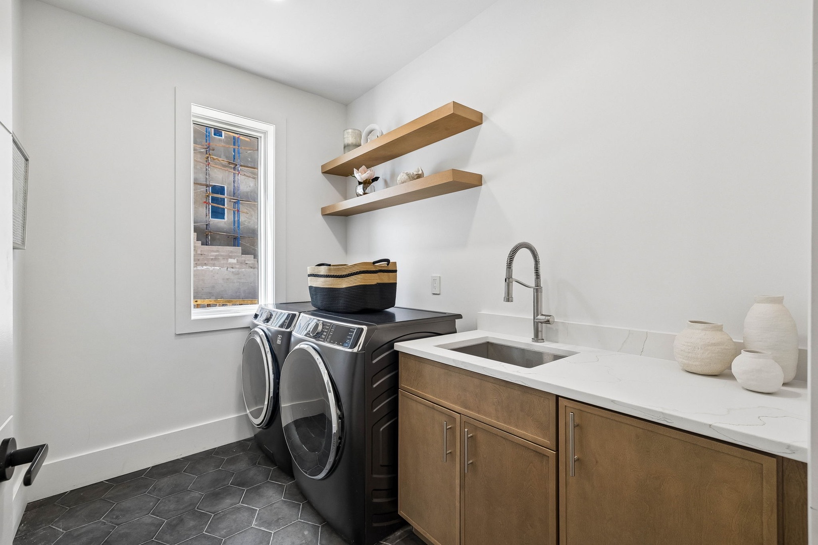 Your laundry room makes chores feel effortless, with sleek countertops, warm wood cabinetry, a deep sink, and open shelving to keep essentials at hand—beautifully designed and completely functional.