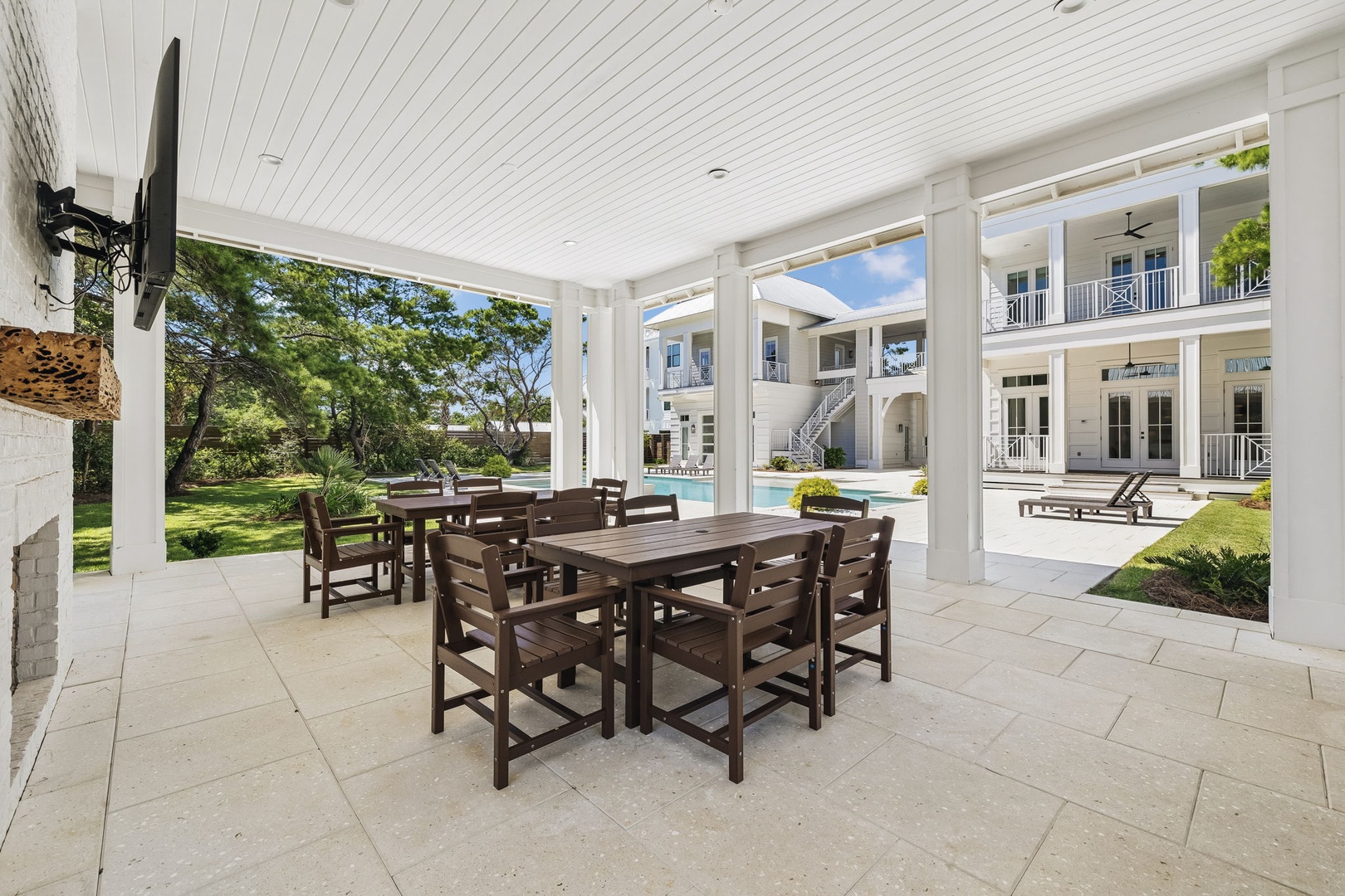 Gather around this spacious covered patio for memorable meals with your group. You'll enjoy the open-air comfort while gazing out at the lush lawn and sparkling pool, all framed by elegant white columns and charming architectural details.
