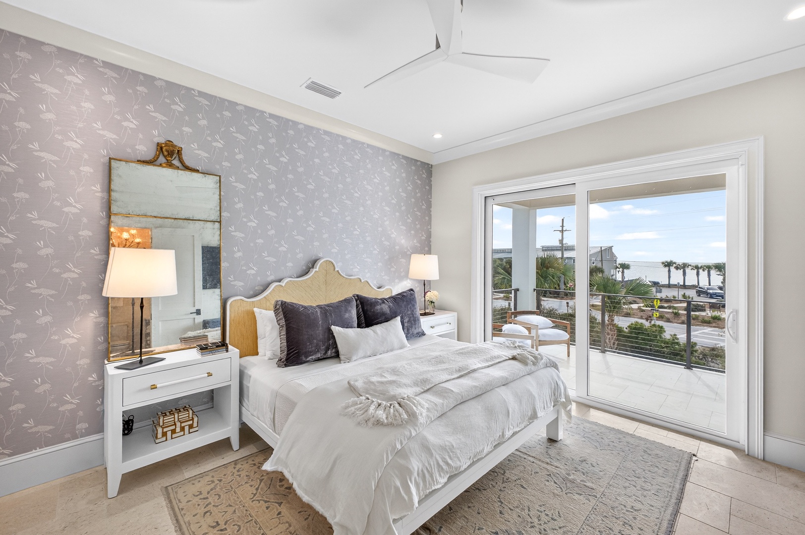 Your elegant bedroom features coastal-inspired wallpaper, a plush bed, and stunning balcony access with tropical views to greet your morning.