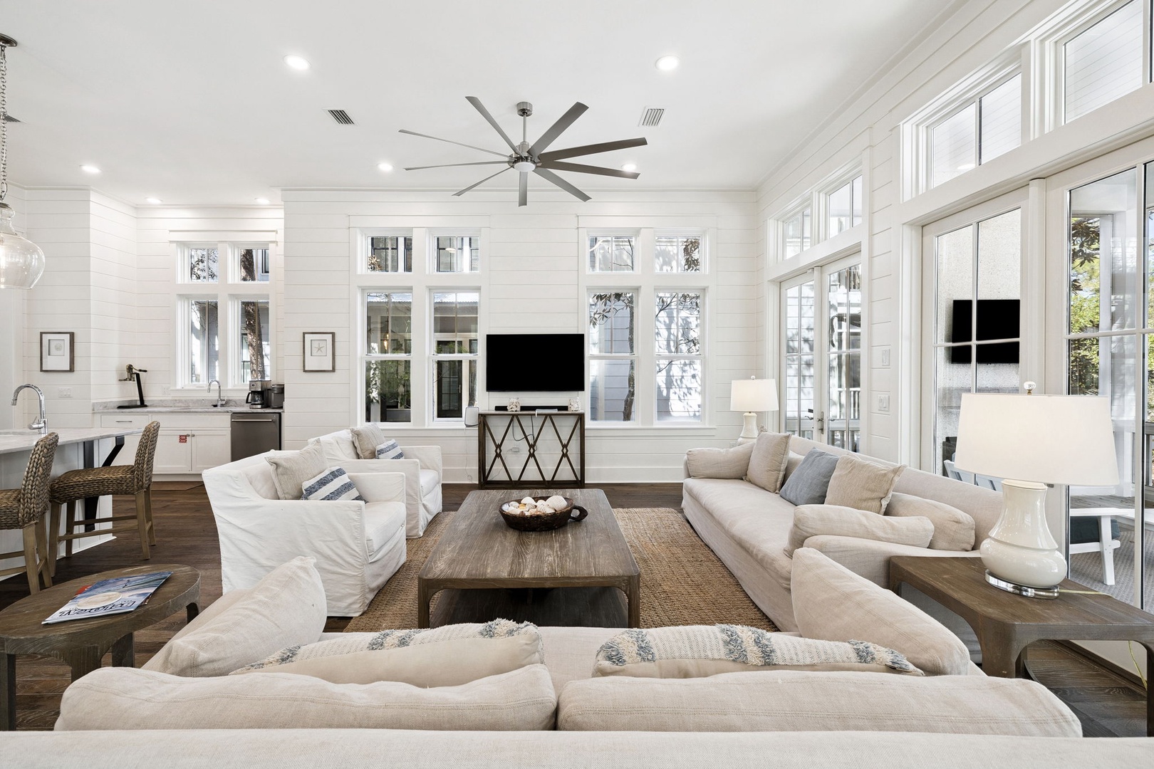 Sink into plush sofas in your bright, airy living space where coastal elegance meets comfort beneath soaring ceilings and oversized windows.