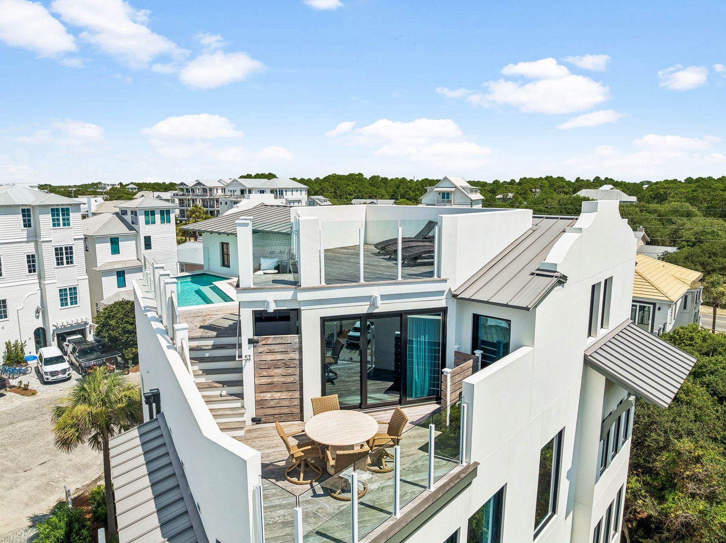 Coastal rental property featuring rooftop terrace with pool, outdoor dining area, and modern architecture nestled among tropical vegetation in a beach community.