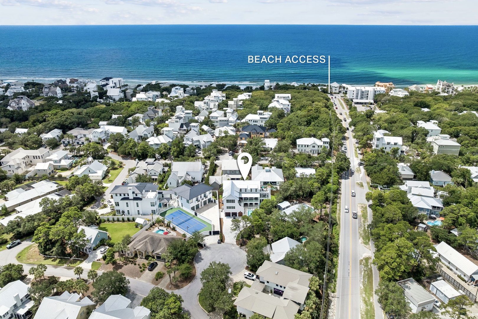 An aerial view showcasing a coastal neighborhood with tree-lined streets leading to pristine turquoise waters and white sand beaches, with convenient beach access nearby.