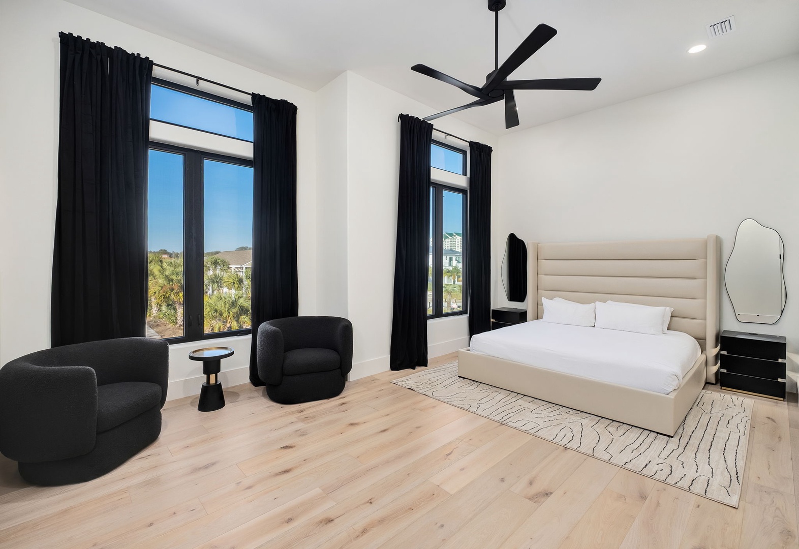 Relax in your modern bedroom with crisp linens, a cozy seating nook, and floor-to-ceiling windows framing tropical views.