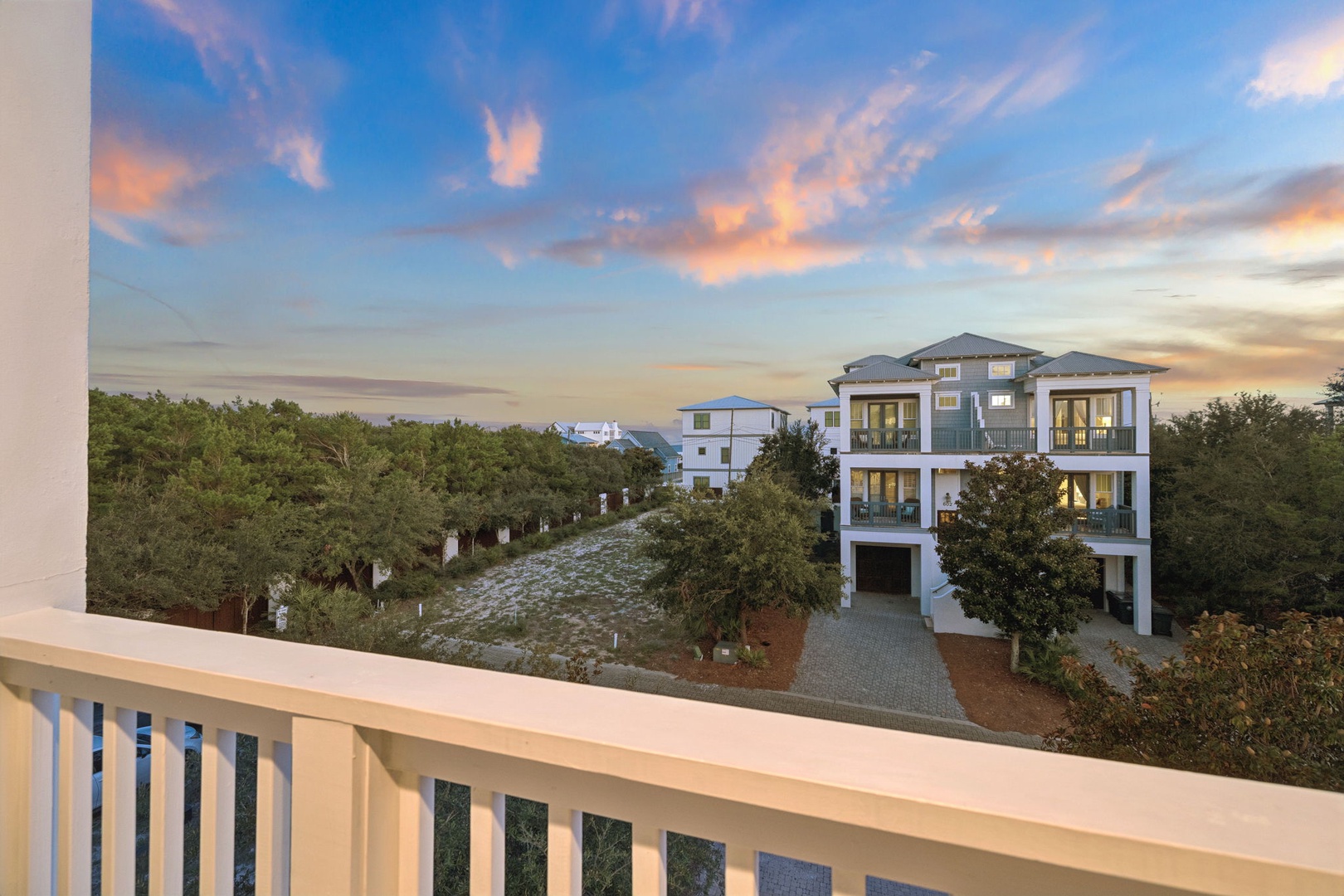 A stunning coastal property surrounded by lush greenery, captured beneath a breathtaking sunset sky painted in soft blues and warm coral hues.