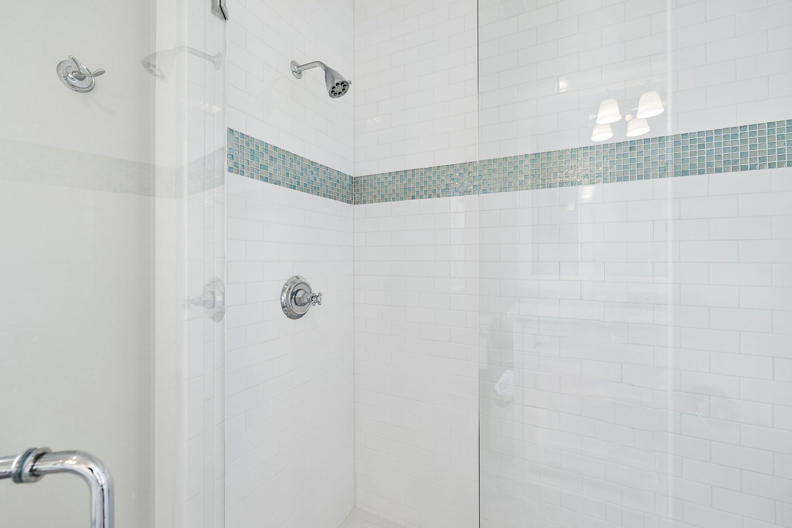Step into a pristine walk-in shower featuring crisp white subway tile accented with coastal-inspired mosaic details and dual rainfall showerheads for your ultimate refresh.