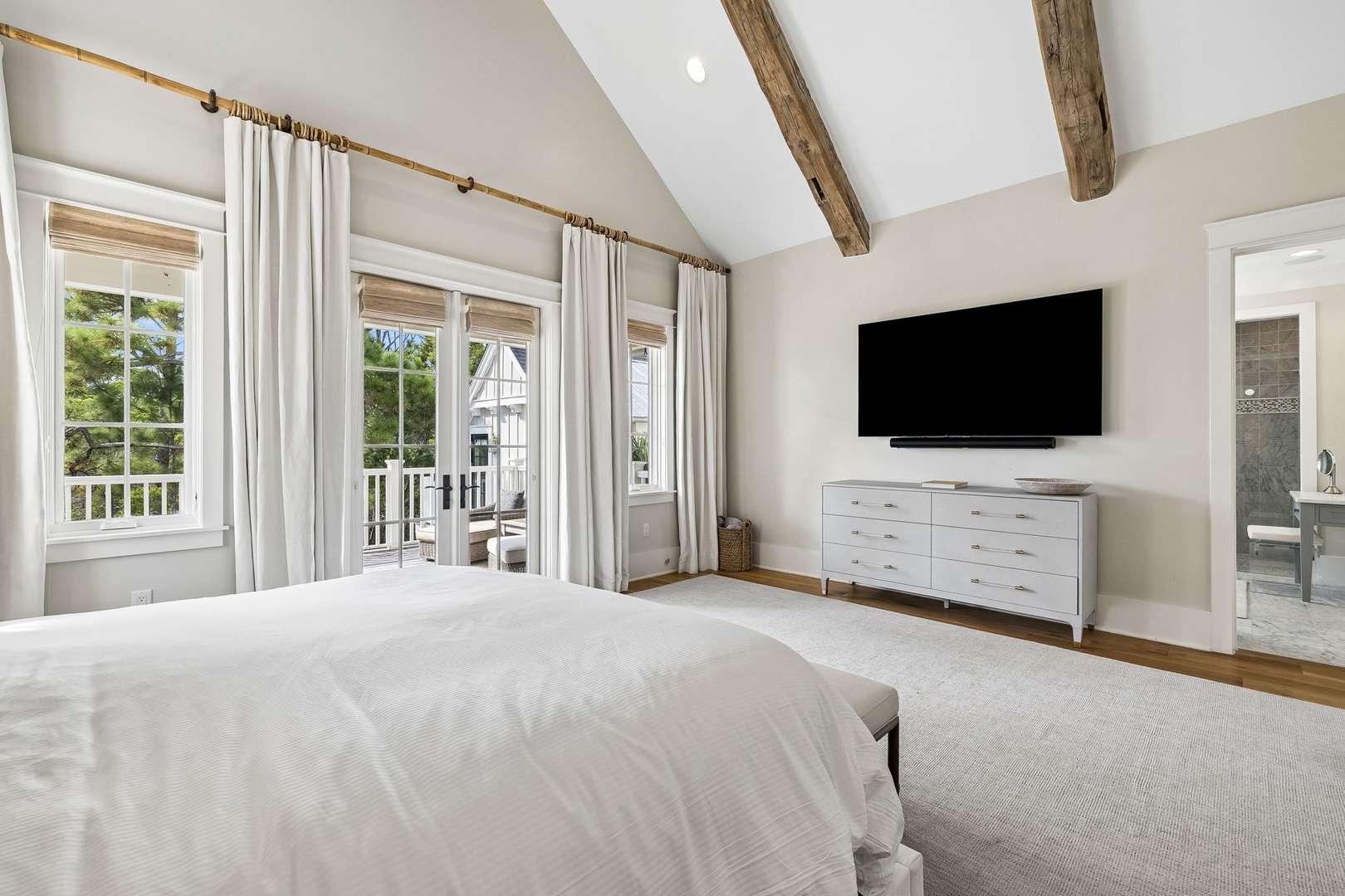 Unwind in your serene master suite where soaring vaulted ceilings with rustic wood beams meet modern coastal elegance. Step onto your private balcony and enjoy peaceful moments in this light-filled retreat.