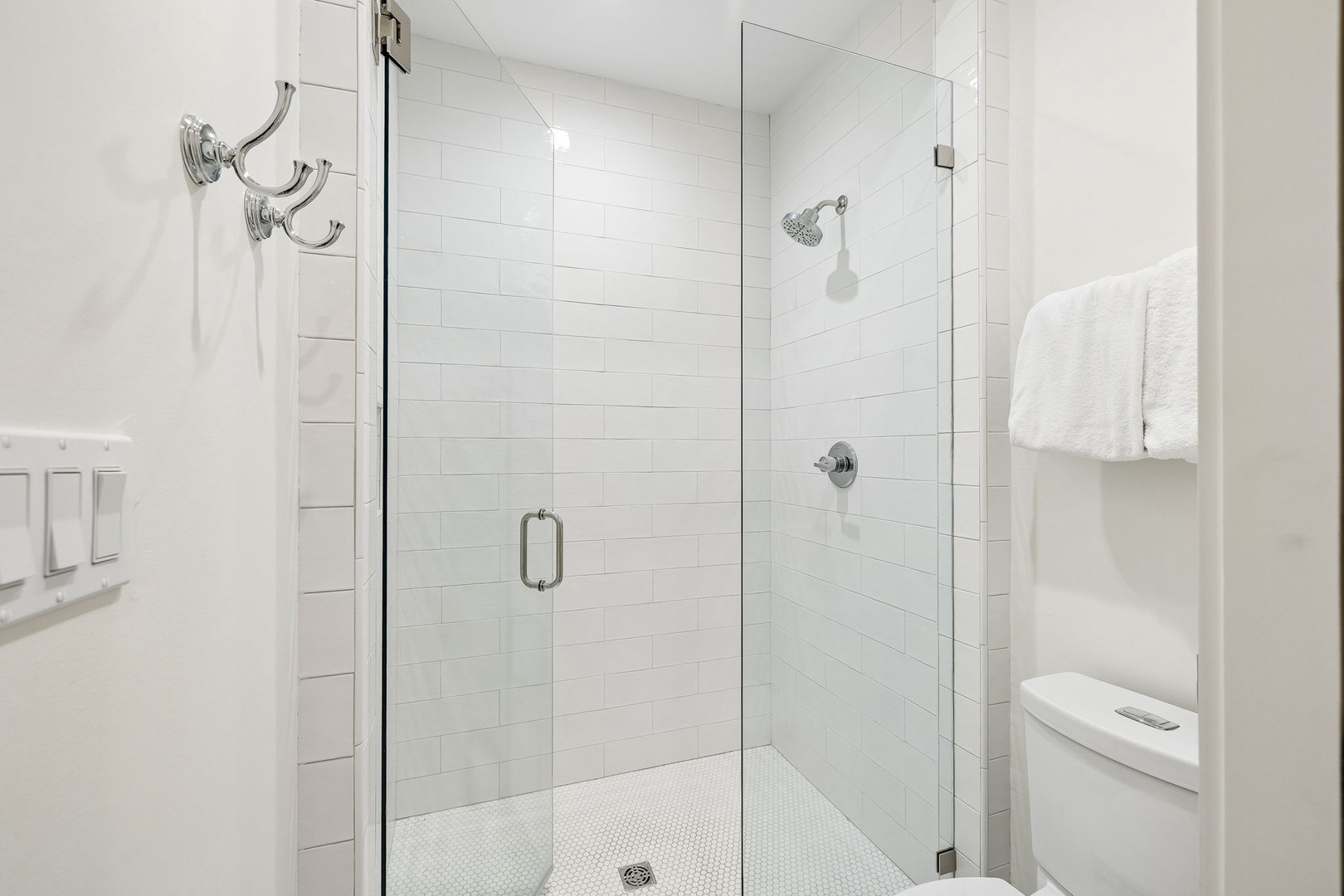 Step into your bright, modern bathroom with a spacious walk-in shower featuring sleek glass doors, pristine white tile, and plush towels waiting for you.