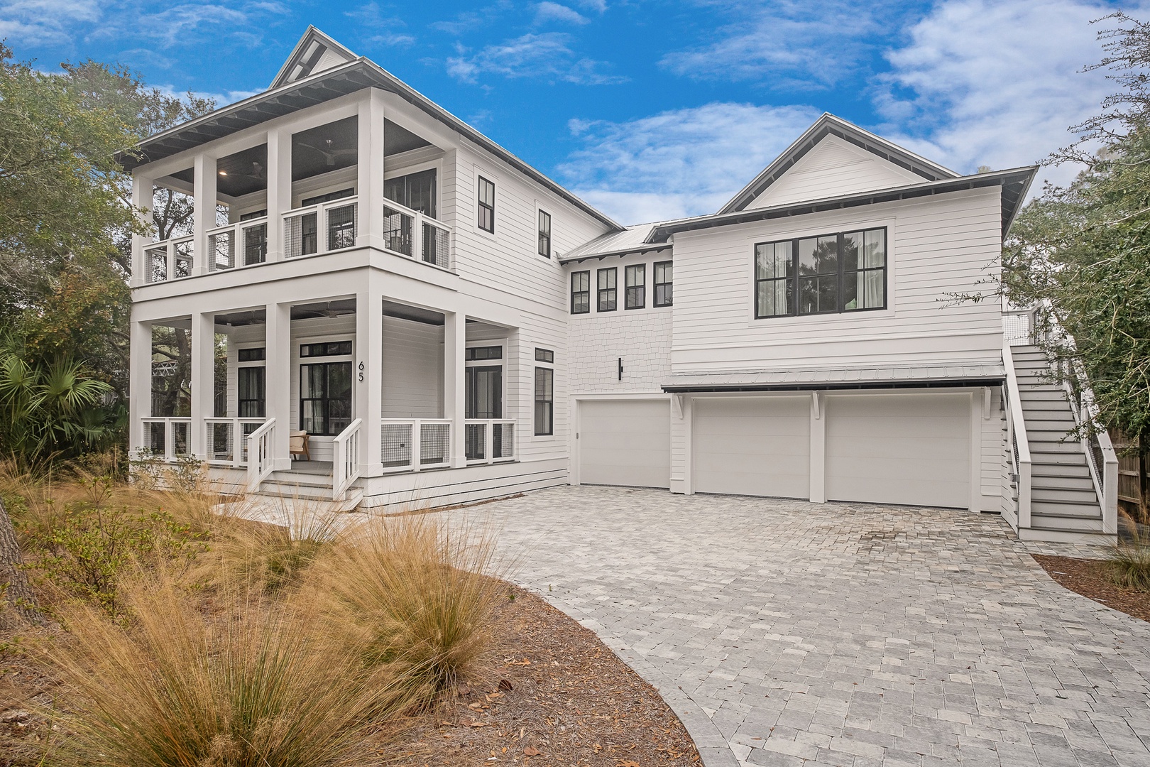 Modern coastal architecture with spacious balconies and pristine paver driveway welcomes guests to this elegant retreat.