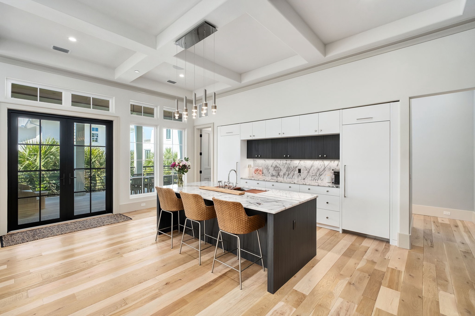 Step into your sleek gourmet kitchen with marble island seating, where morning coffee and evening conversations flow naturally beneath soaring coffered ceilings.