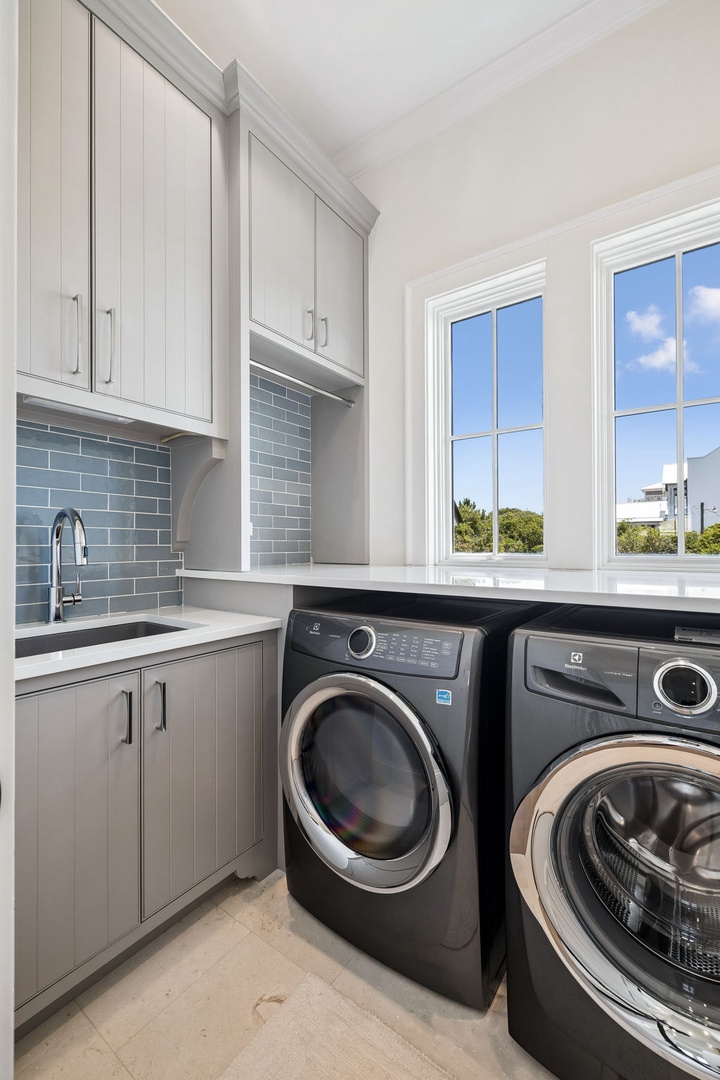 A bright and immaculately designed laundry room awaits, with custom cabinetry, elegant tile backsplash, and high-end appliances that make chores feel effortless during your stay.