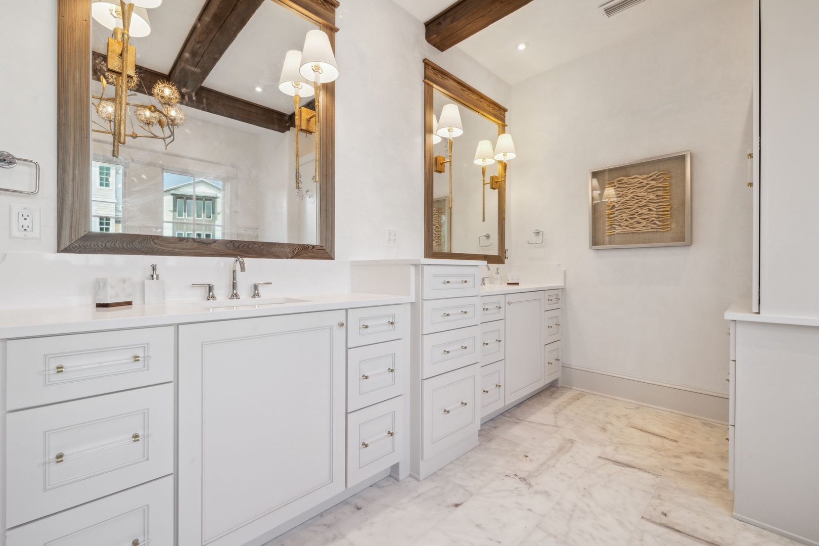 Step into your tranquil ensuite featuring dual vanities with crisp white cabinetry, elegant exposed wood beams overhead, and ample natural light reflecting off pristine marble-look flooring for a truly serene retreat.