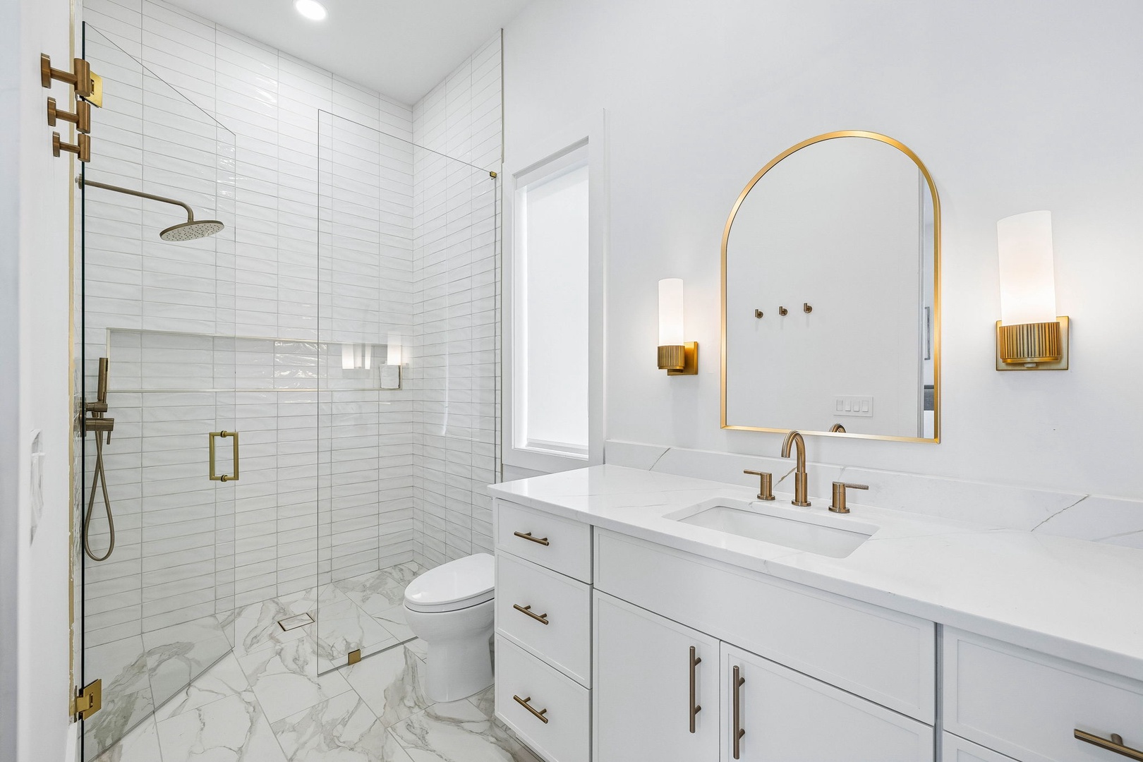 Bright, spa-inspired bathroom with elegant gold accents, marble floors, and a spacious glass-enclosed shower where you can refresh and unwind in style.