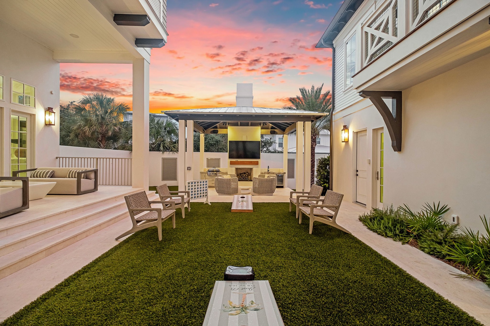 An elegant courtyard offers the perfect setting for relaxation or socializing beneath a stunning sunset, with plush seating, lush lawn, and a covered outdoor kitchen awaiting your arrival.