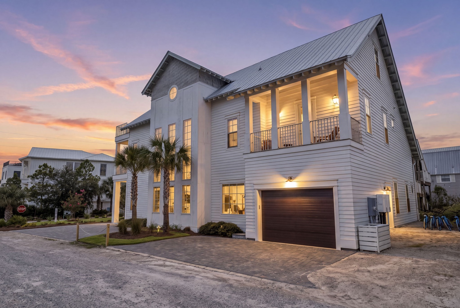 A striking coastal-style home showcasing modern architecture with warm lighting as the sun sets over the neighborhood.