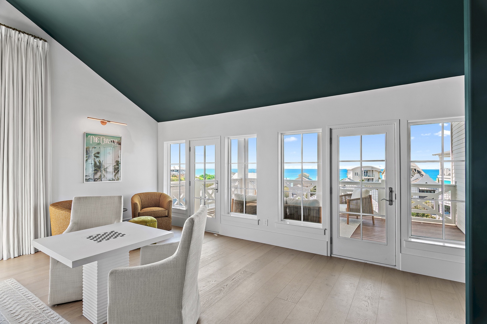 Step into your bright, airy living room where ocean views greet you through floor-to-ceiling French doors. Sink into cozy seating beneath a bold teal ceiling and feel the coastal breeze beckoning you outside.