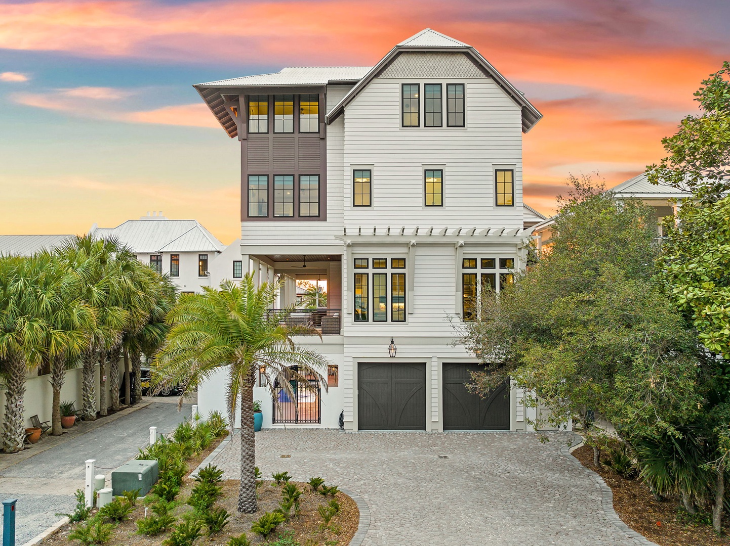 A stunning coastal property showcasing modern architecture against vibrant sunset skies, surrounded by lush tropical landscaping and palm trees.