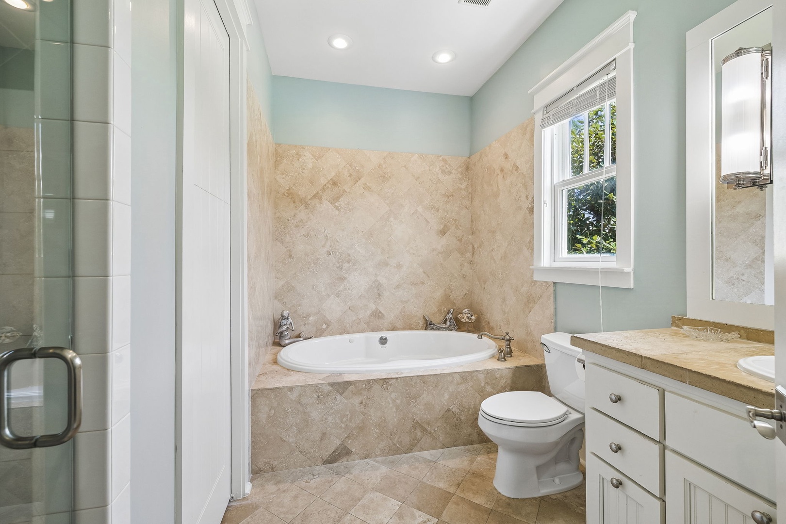 Unwind in your serene spa-like bathroom with a soaking tub framed by warm travertine and soft aqua walls. Natural light fills the space, making it the perfect retreat after a day of exploring.