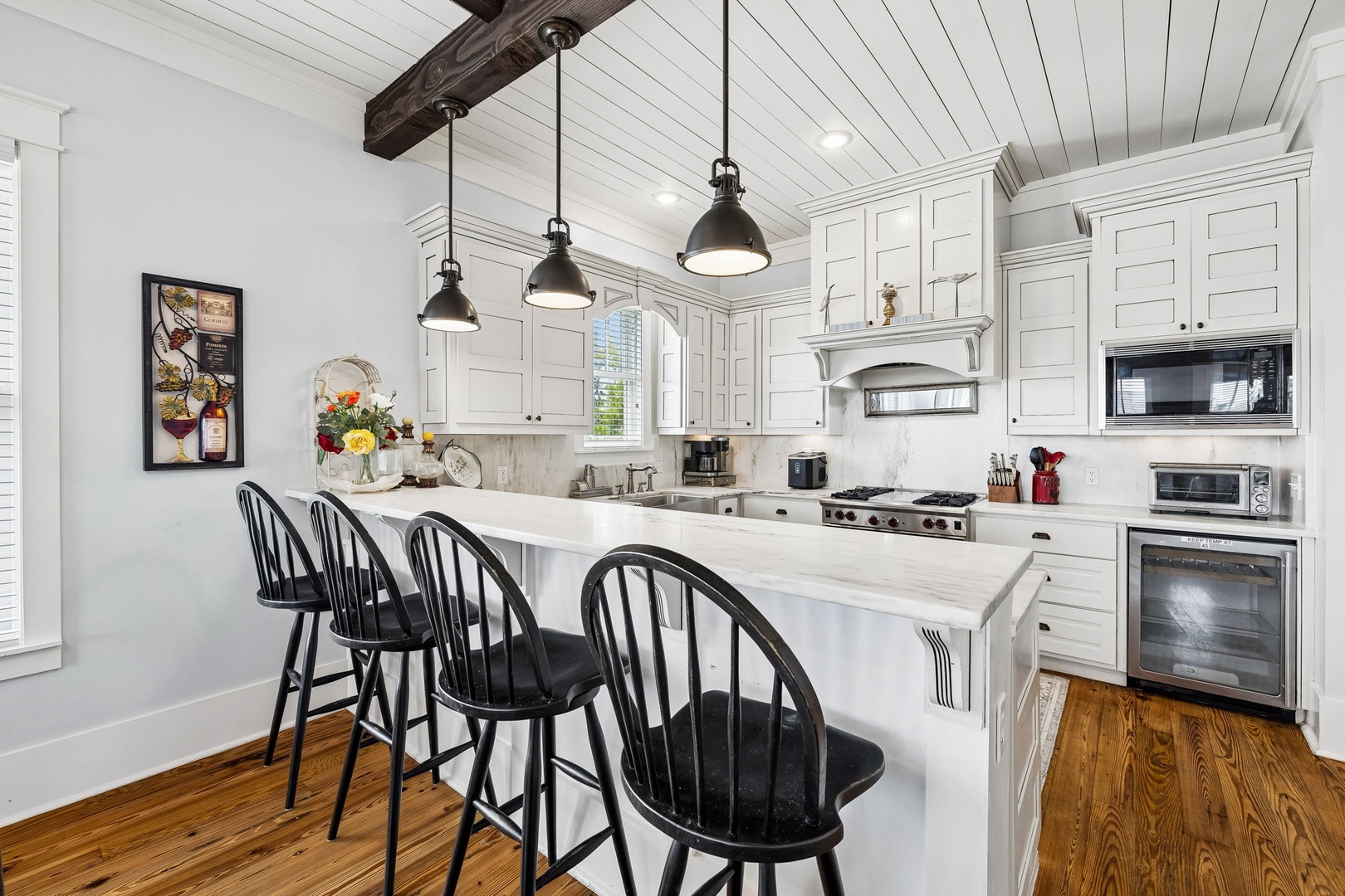 Your beautifully appointed kitchen awaits, with white cabinetry, a welcoming island with seating, and a rustic wooden beam overhead. Gather here to prepare meals and share stories together.