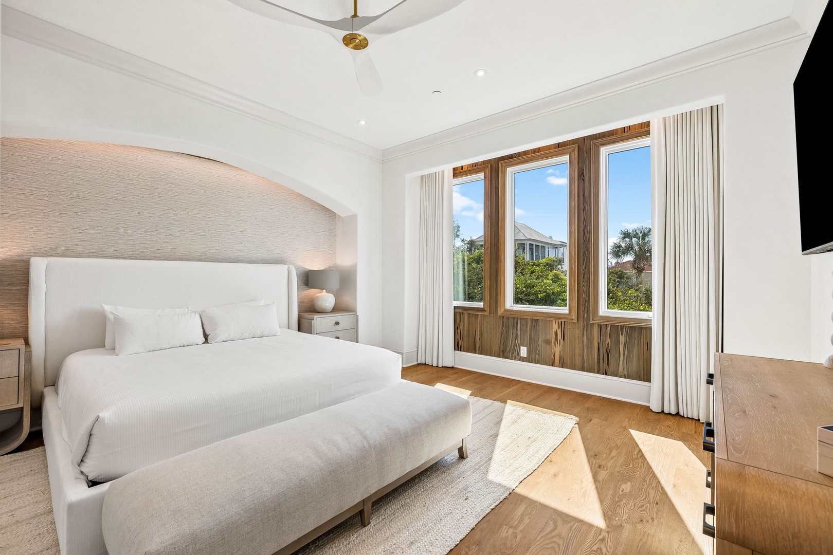 Wake up in this serene bedroom where natural light pours through expansive windows framing lush coastal views. Relax on plush bedding in your peaceful retreat.