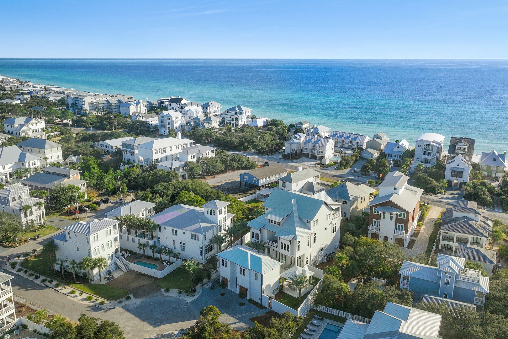 Aerial view of a charming coastal neighborhood where colorful beach homes nestle between lush greenery and pristine turquoise waters, showcasing a peaceful Gulf Coast community.