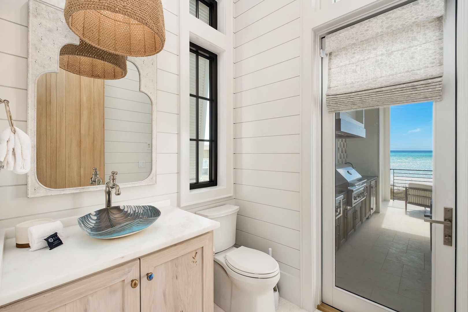 Coastal elegance meets comfort in your private bathroom, featuring a stunning glass vessel sink and natural woven light fixture that perfectly complement the serene beachside setting.