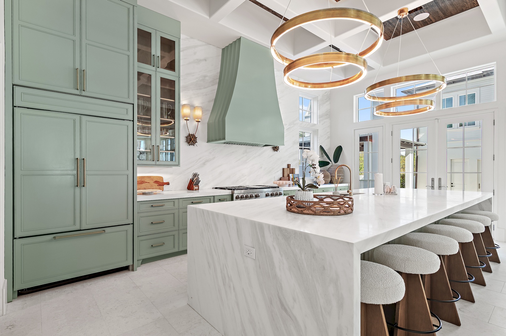 Imagine cooking in this stunning kitchen with sage cabinets, marble backsplash, and a gleaming island perfect for gathering. Natural light pours through French doors, inviting you to relax and enjoy your stay.