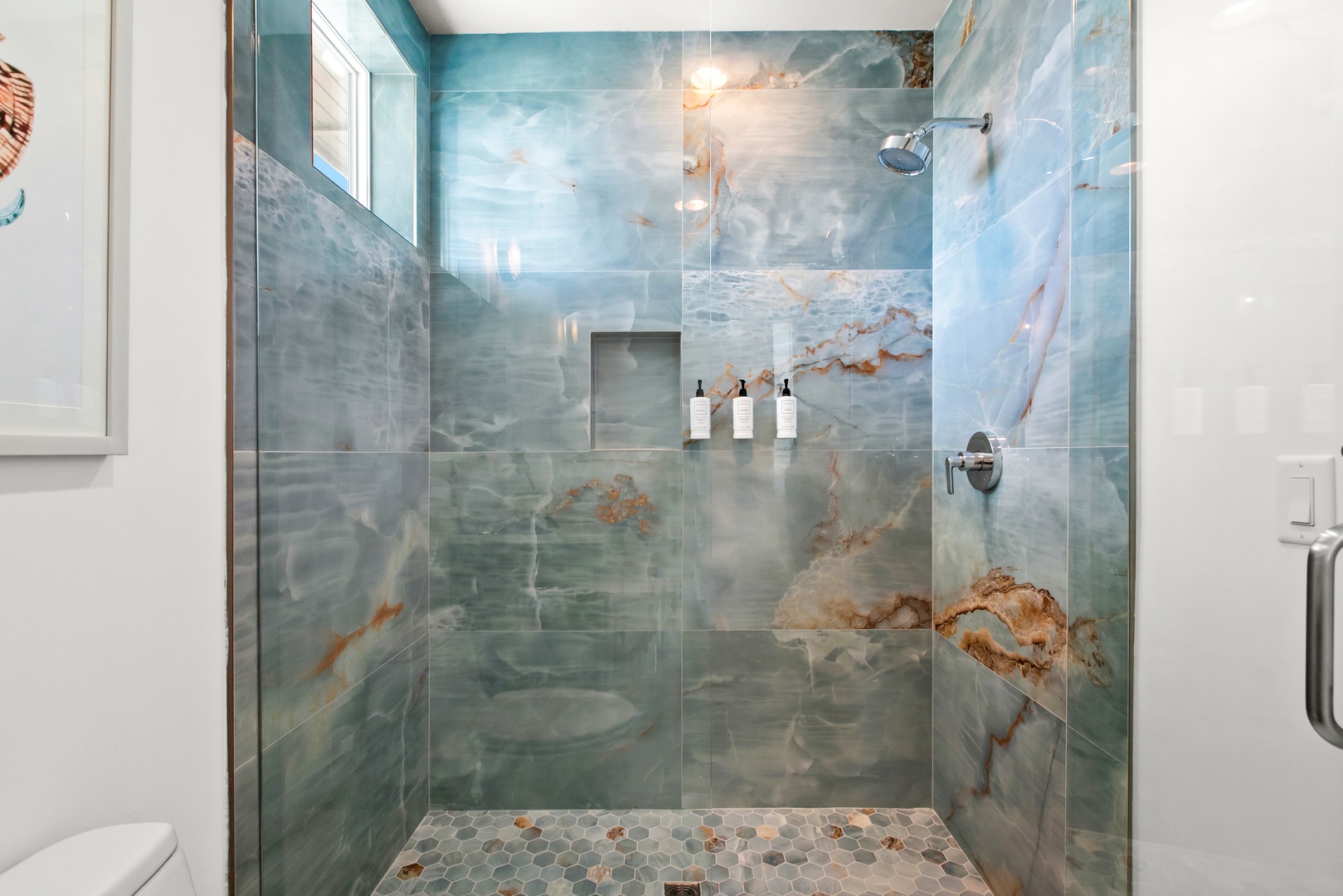 Artisan tile in soft ocean hues wraps your spacious walk-in shower, where a built-in niche holds essentials and a rainfall showerhead promises a calming retreat after your day.