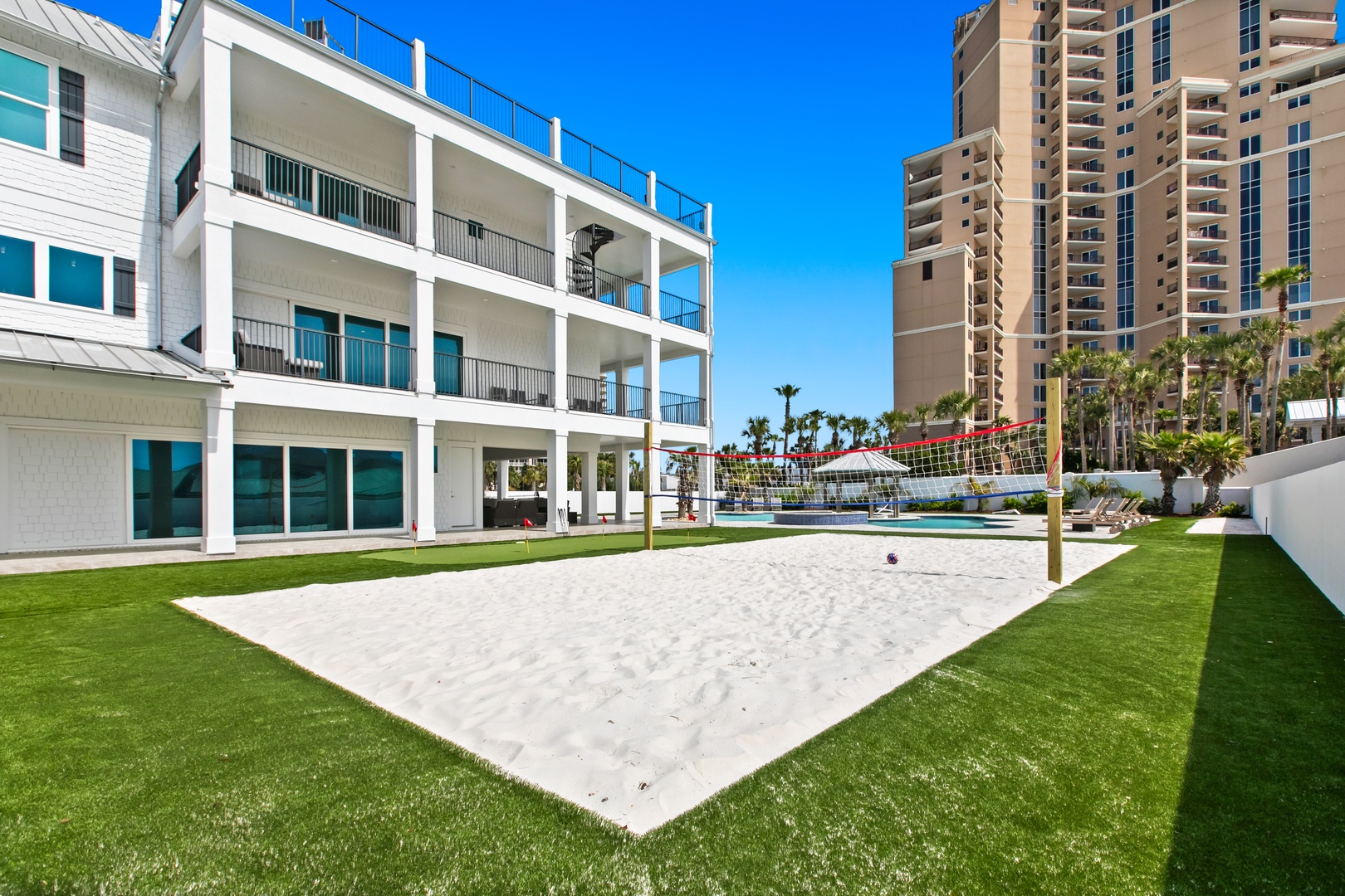 A private beach volleyball court awaits your friendly matches, surrounded by lush artificial turf and swaying palms—ideal for sunny competitions or barefoot fun between dips in the pool.
