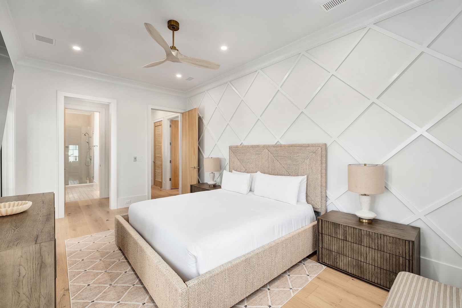 Relax in your serene bedroom featuring a plush king bed, elegant geometric wall design, and ceiling fan for perfect temperature control.
