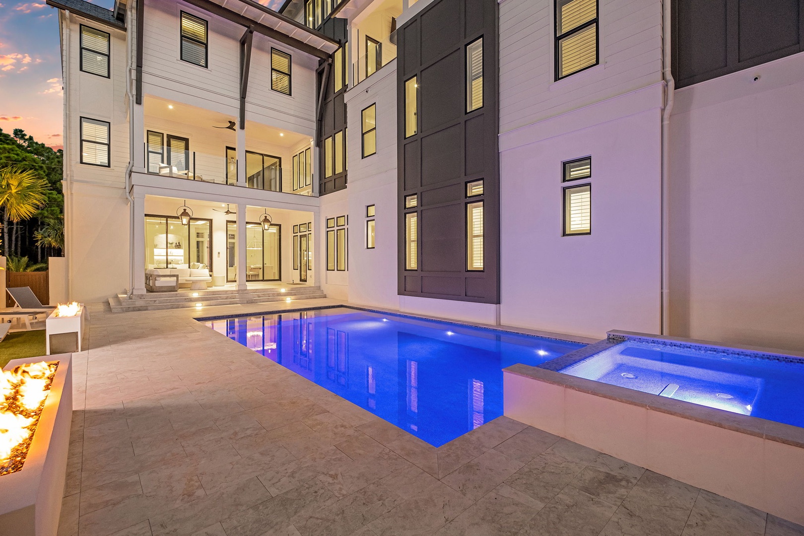 This modern vacation home features a stunning courtyard with an illuminated pool and hot tub. Elegant architecture surrounds the private outdoor space, perfect for evening relaxation.