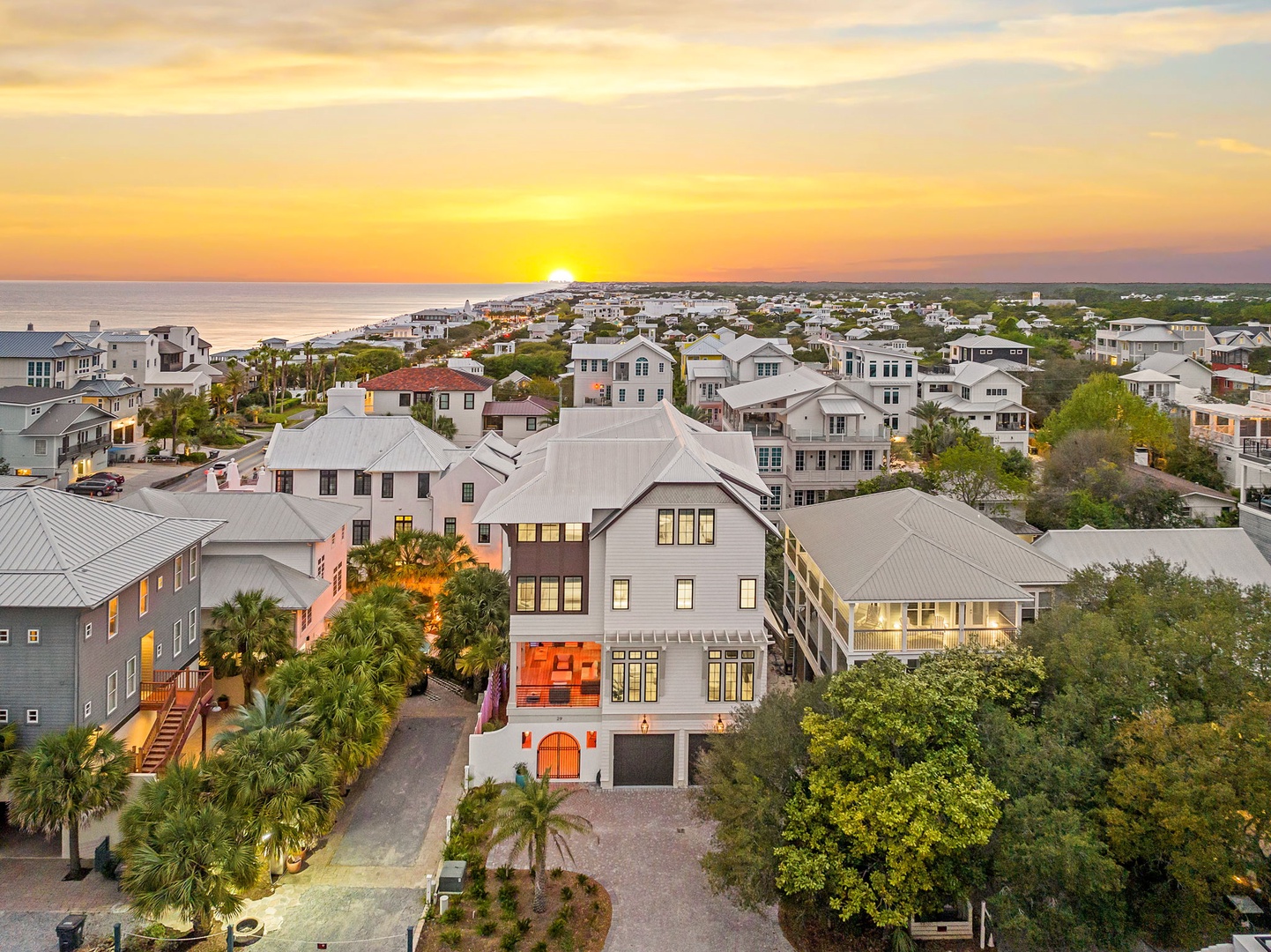 Stunning aerial view of a coastal community at sunset, showcasing beachfront properties nestled among lush palm trees and mature landscaping.