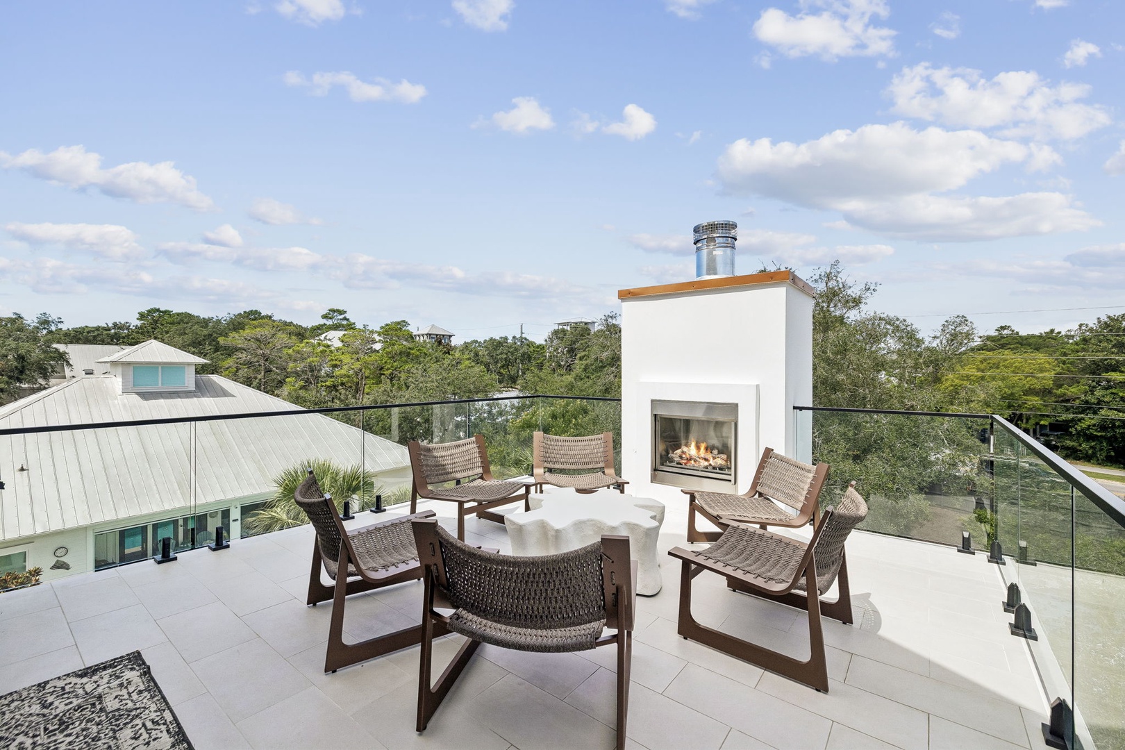 This rooftop terrace offers a serene escape with modern outdoor seating arranged around a contemporary fireplace, all framed by lush treetop views and open sky.