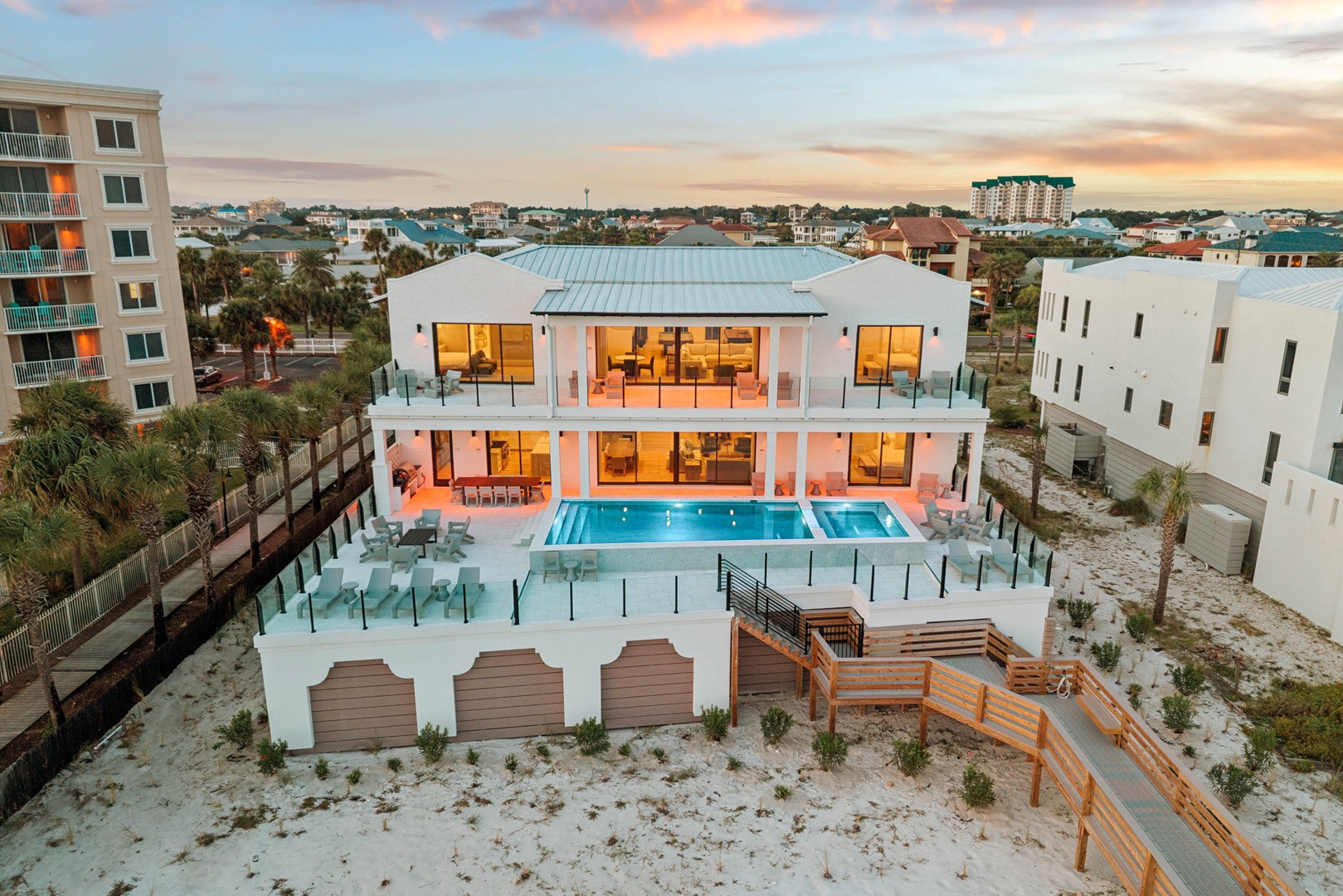 A stunning modern beach house with expansive decks, a sparkling pool, and beautifully lit interiors, set against a peaceful coastal neighborhood at sunset.